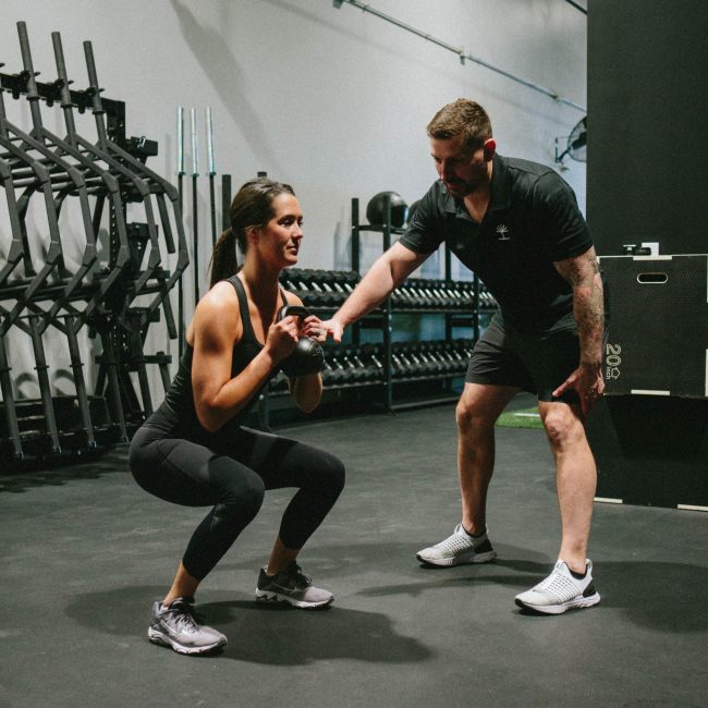 Personal trainer works with female client on kettle bell squat depth
