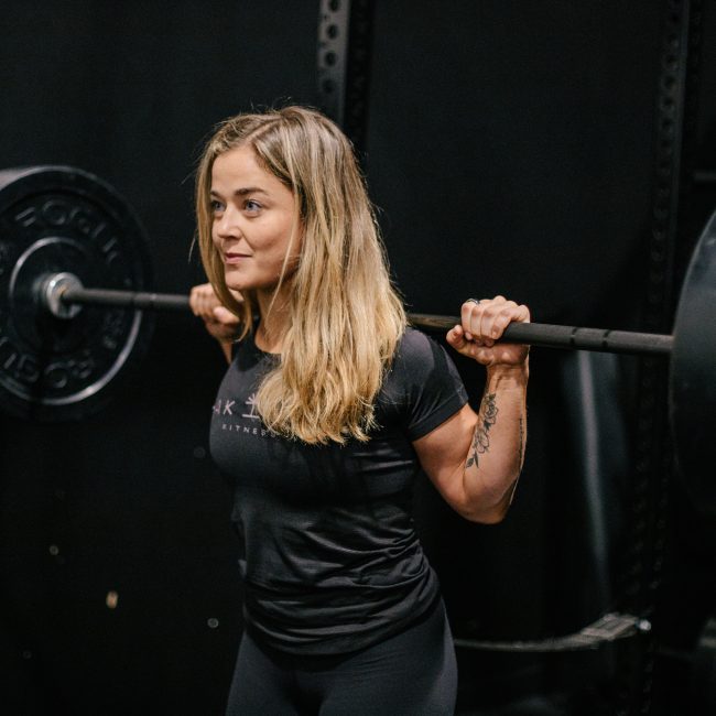 Rachel Nicholson, CSCS certified strength coach and personal trainer with a barbell racked across shoulders